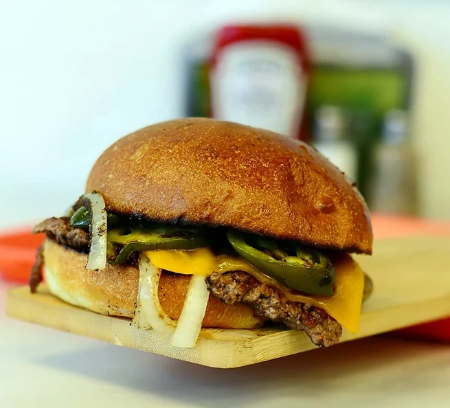 Smash burger with grilled jalapenos, onion and cheddar on a wooden board